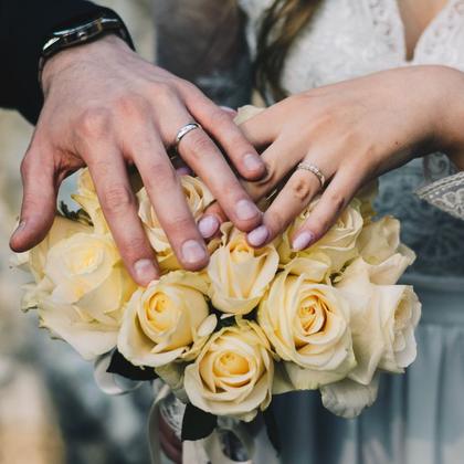Hands and rings above a bouquet of yellow roses.
