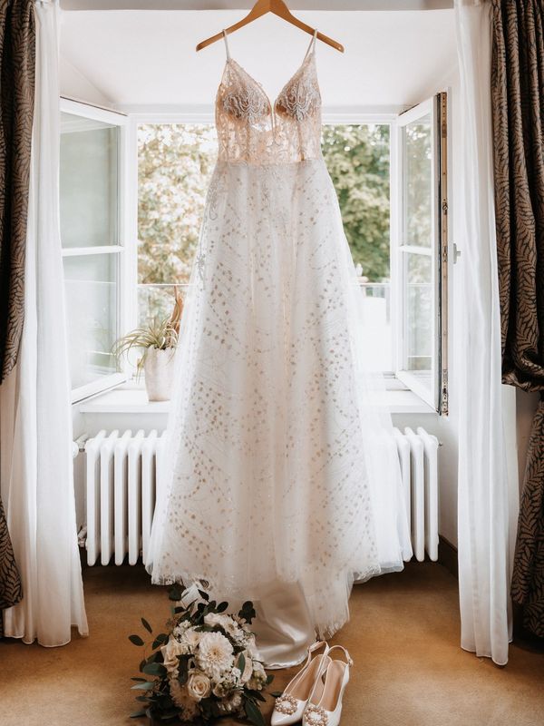 A wedding dress hanging in the light of a tall window.