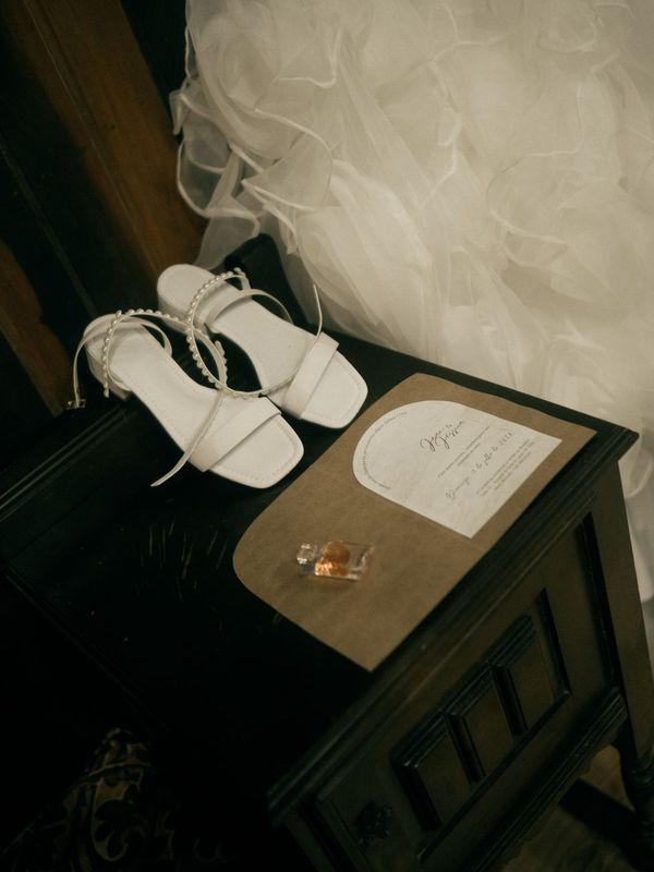 Shoes and a printed invitation arranged on a dark nightstand.
